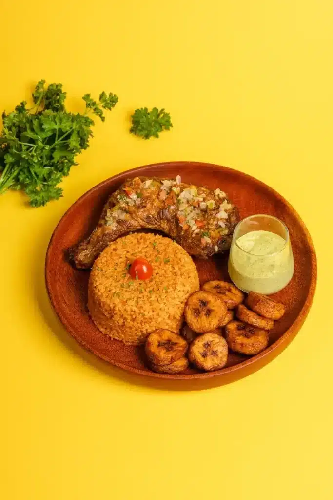 Grilled chicken served with jollof rice, fried plantains, and green sauce at Afrogood Lausanne