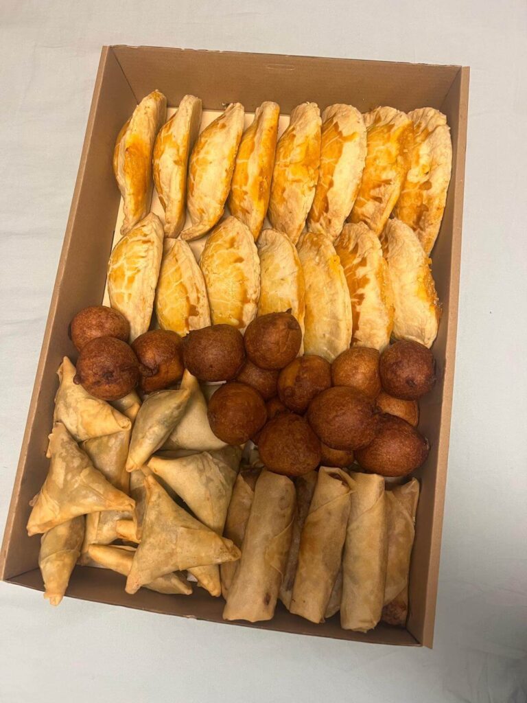 Selection of homemade African snacks including meat pies, samosas, spring rolls, and puff-puff prepared by AfroSwiss Cuisine Geneva