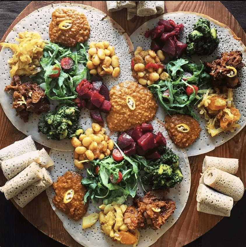 Mixed East African injera platter with chickpeas, vegetables, beef dishes, and traditional Ethiopian and Eritrean flavors