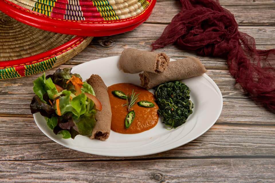 Homemade Eritrean beef stew served with traditional injera platter and fresh vegetables at Raena Lucerne