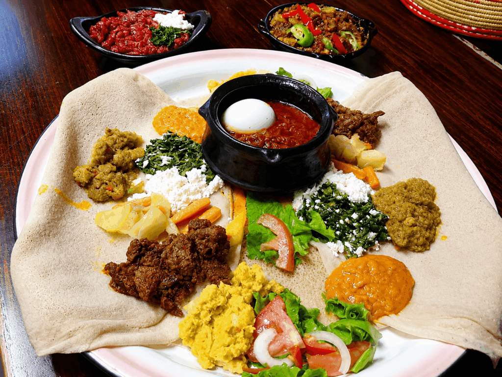 Authentic Habesha mixed platter with injera, traditional stews, vegetables, homemade cheese, and spicy egg stew served at Restaurant Marathon