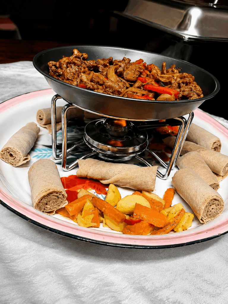 Sizzling Tibs specialty with grilled meat, vegetables, and traditional injera rolls showcasing authentic Eritrean and Ethiopian cuisine at Restaurant Marathon