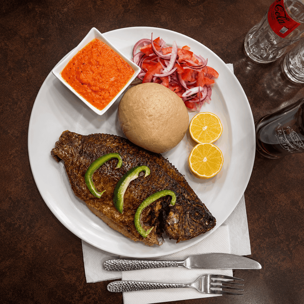 Traditional Nigerian fried fish served with Fufu, fresh vegetables, and homemade pepper sauce at Queen Idia Restaurant Zürich